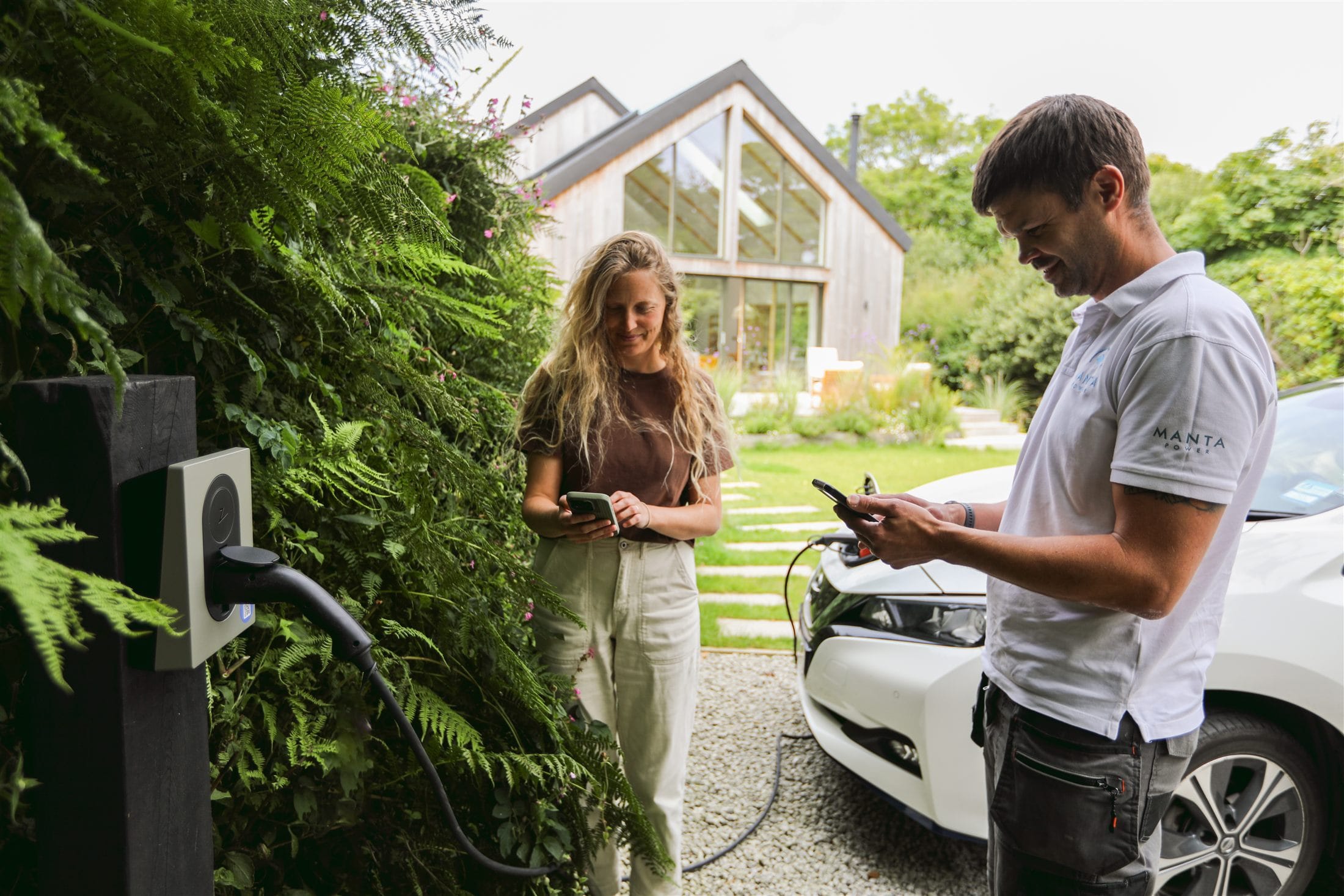 A holiday-let guest paying for charging on her phone, beside a charger on a timber post, with the car plugged in